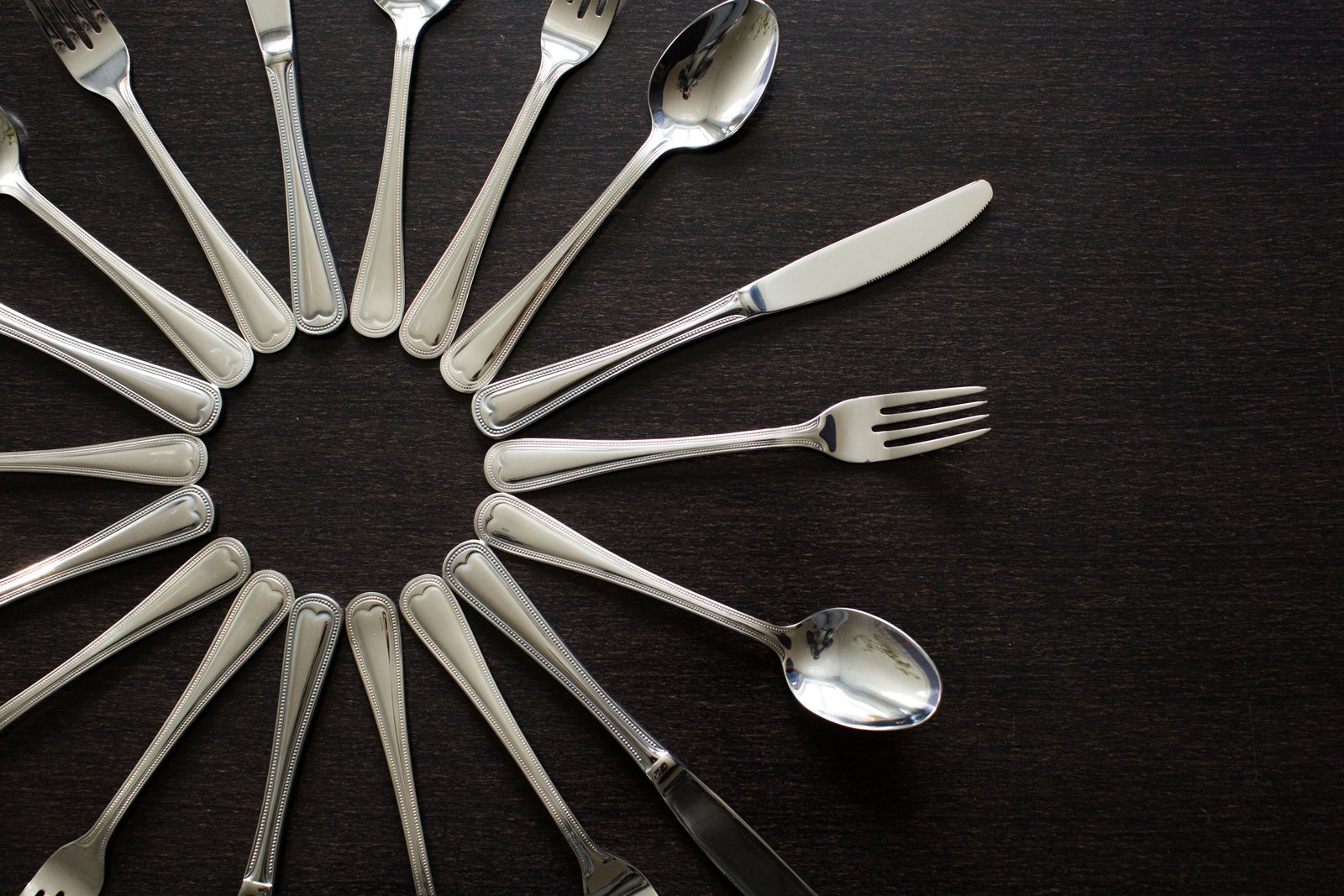 Polished stainless forks, knives, and spoons arranged radially, highlighting consistent surface finishing and reflection quality.