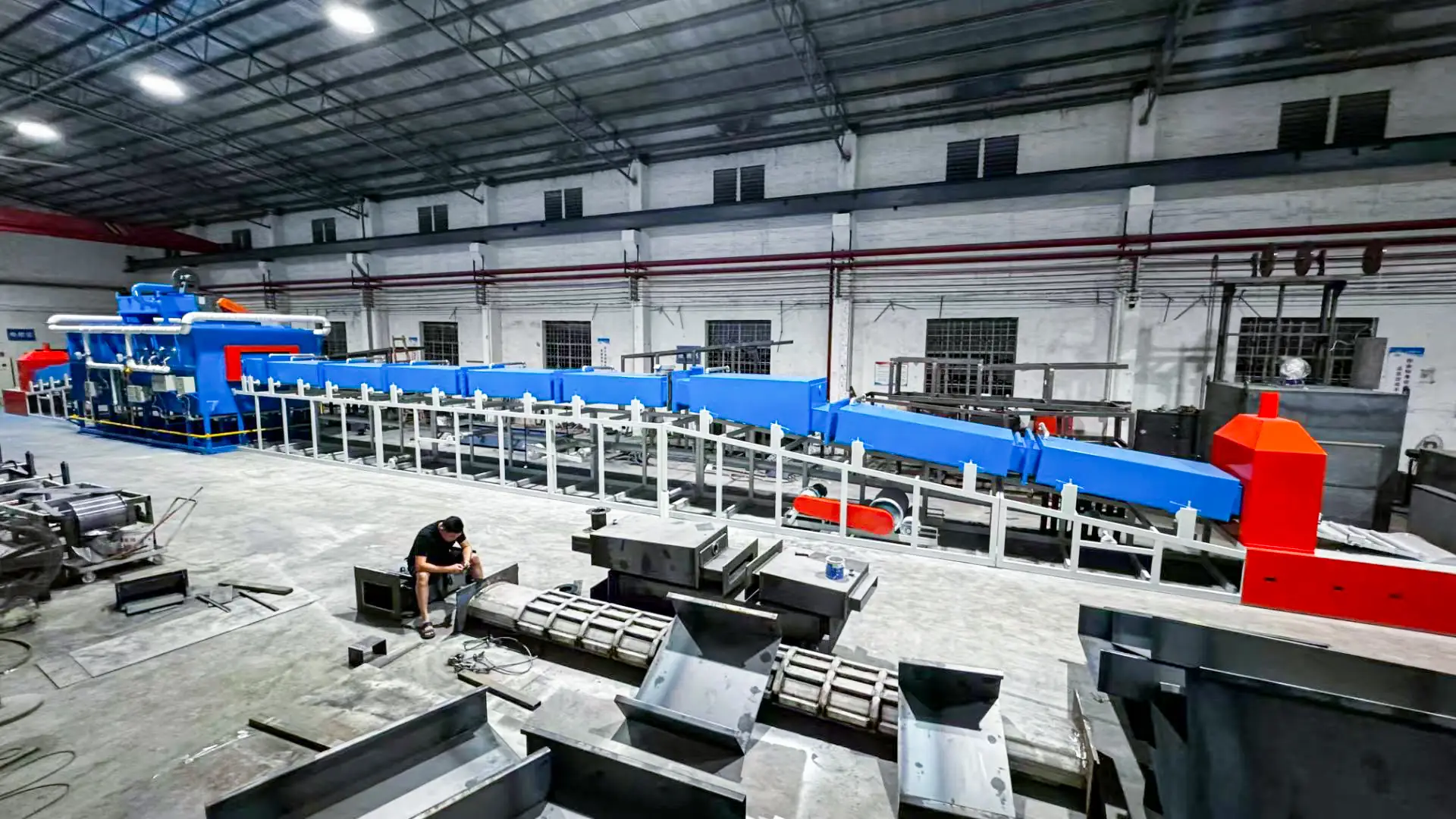 Large blue and red annealing furnace in a factory setting with a worker nearby