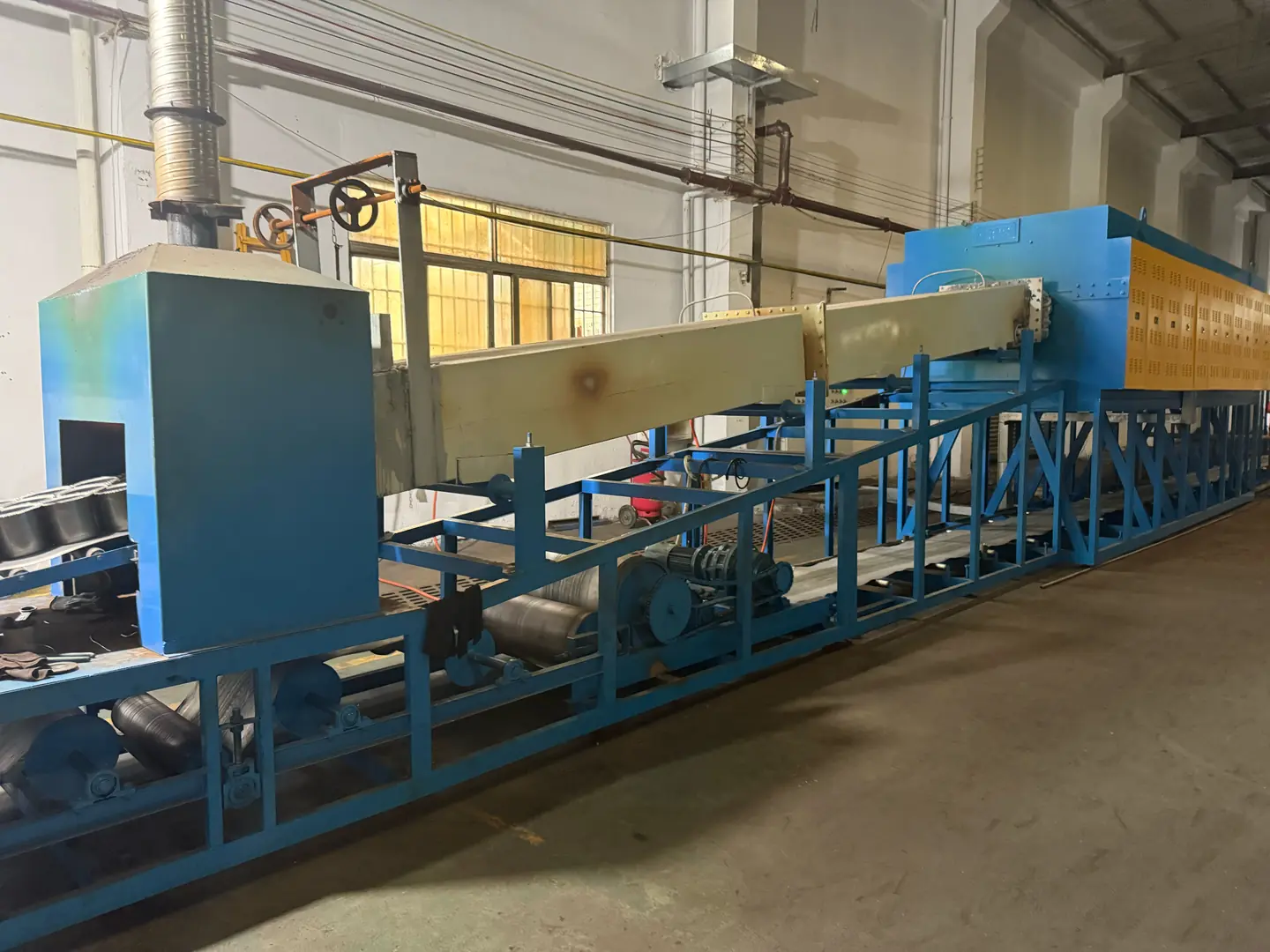 Large blue heat treatment furnace in industrial setting with conveyor belt and control systems
