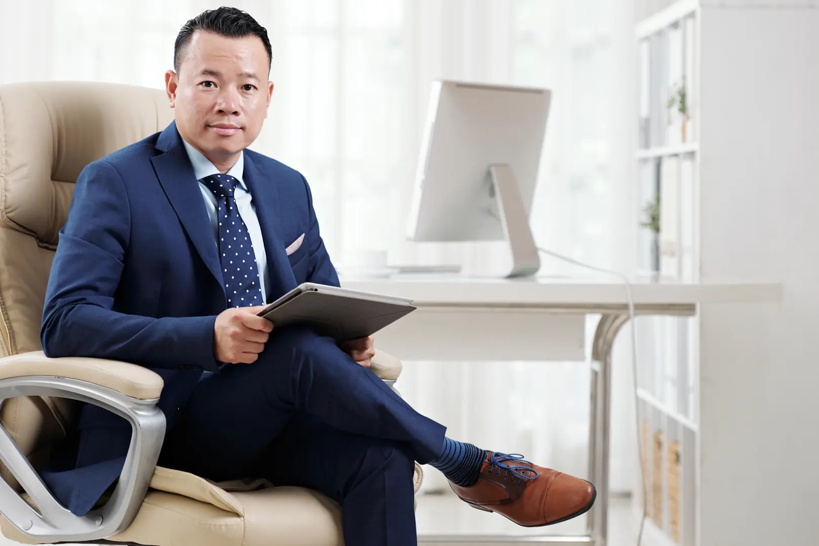 Businessman in navy suit sitting with tablet in modern office